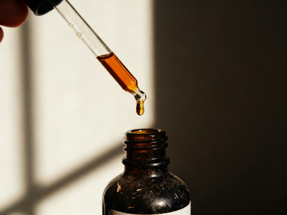 A droplet of amber oil falling from a glass pipette into a dark bottle.